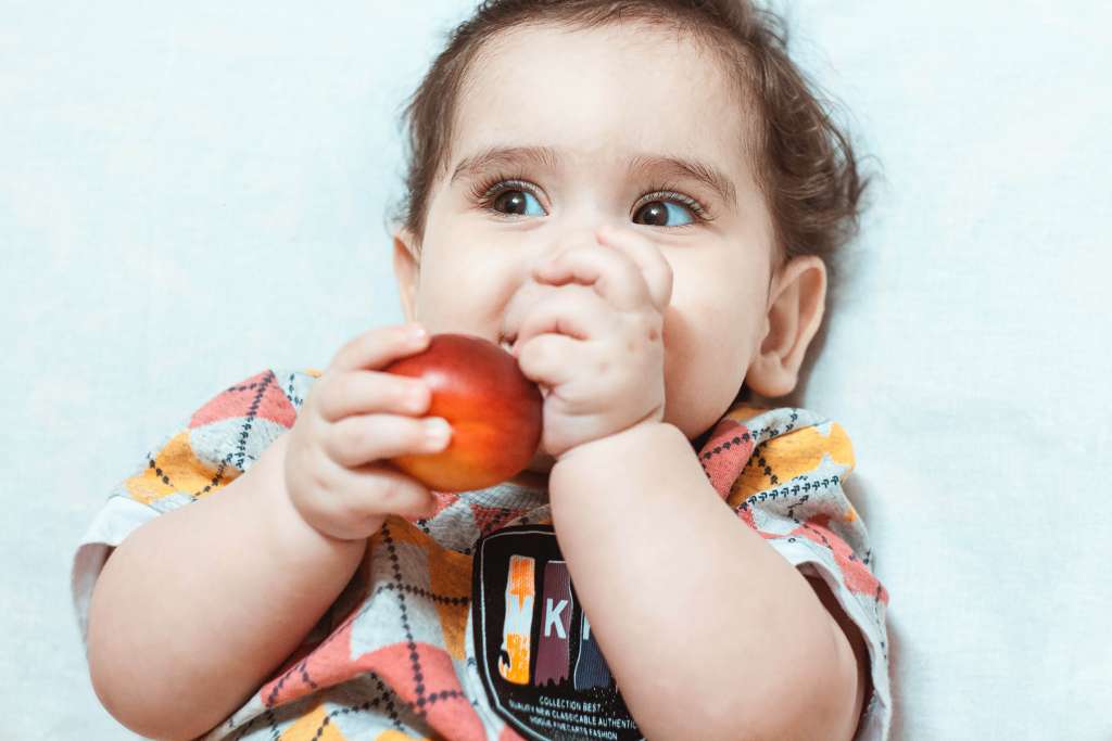 bebê deitada com fruta na mão