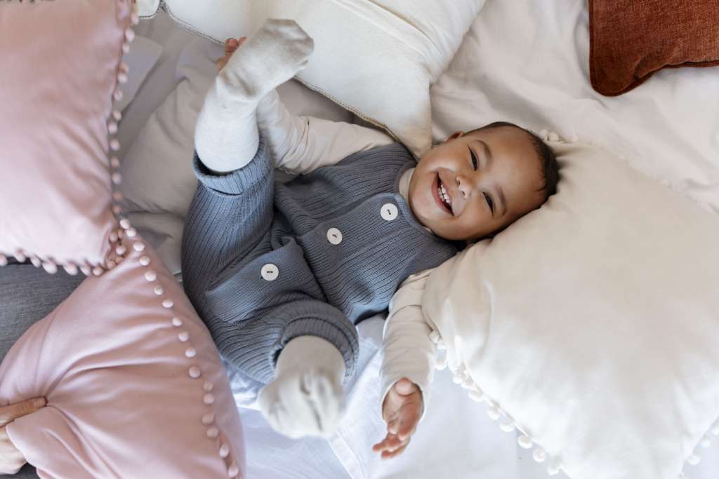 bebê sorrindo deitada na cama com pernas para cima