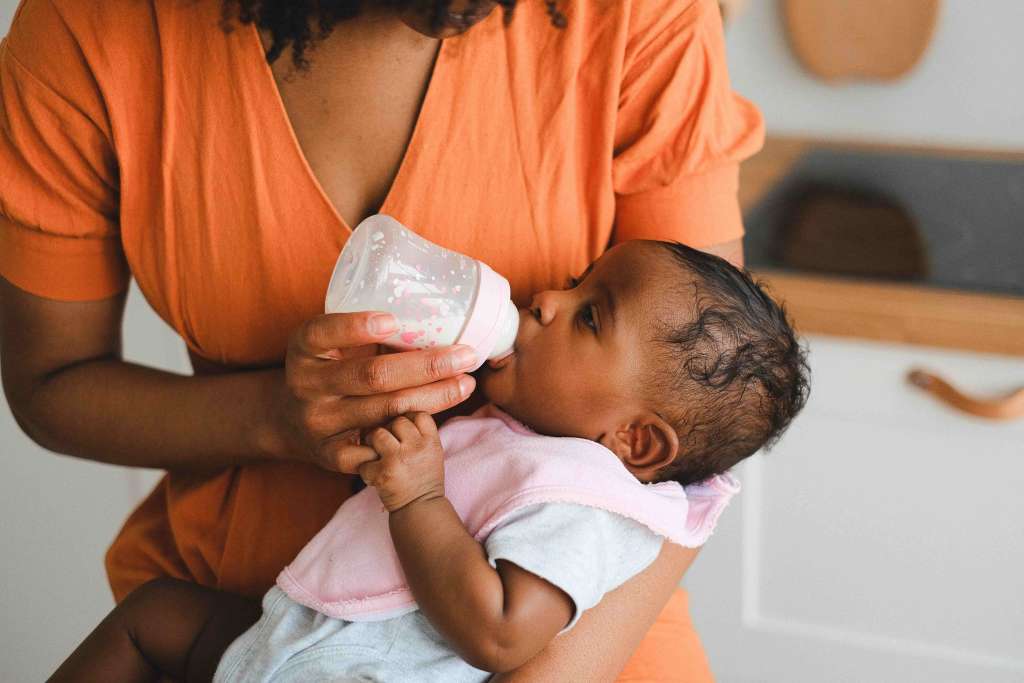 criança mamando mamadeira no colo da mãe.