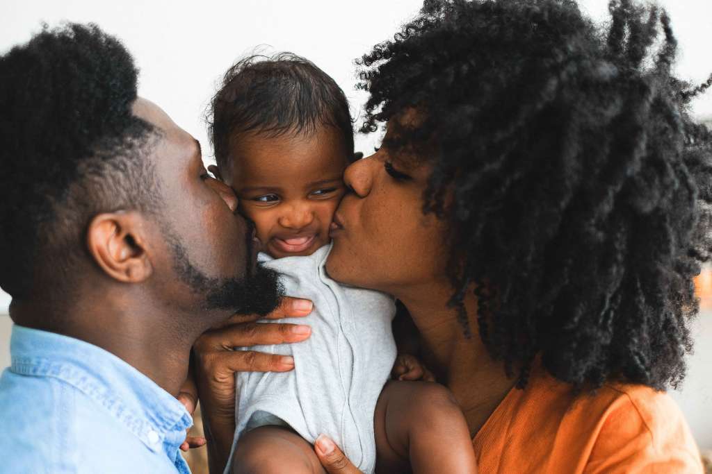 pai e mãe beijando o filho na bochecha.