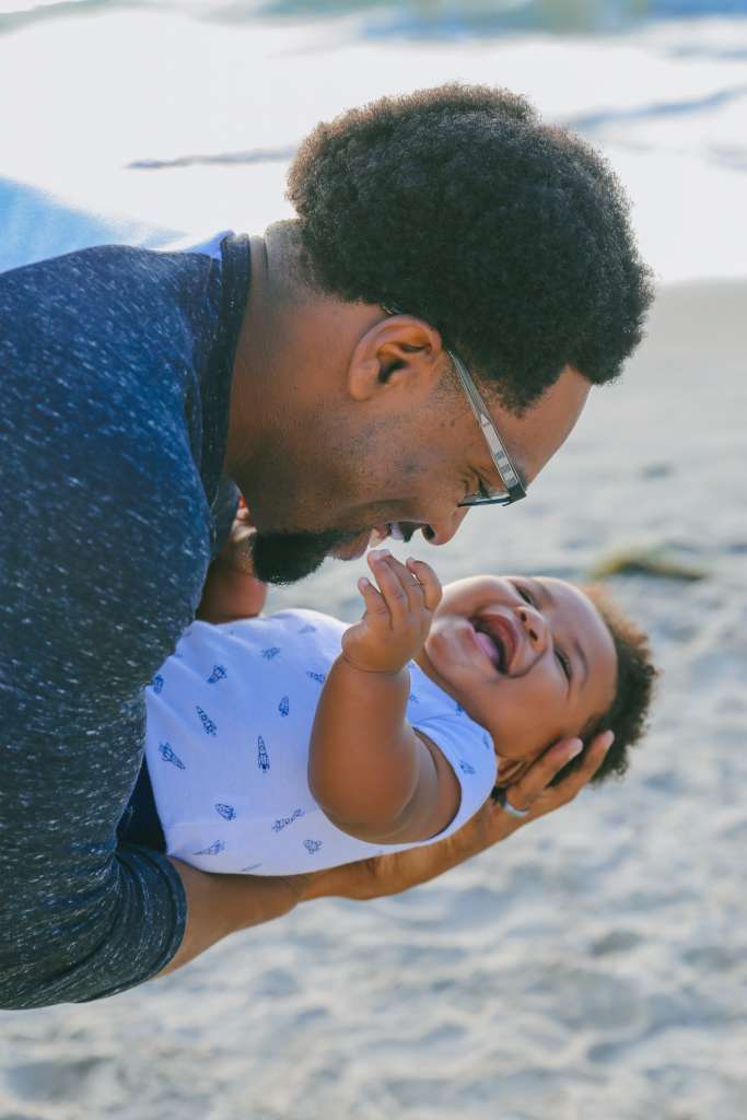 pai segurando o filho que está sorrindo mostrando os dentes de leite.