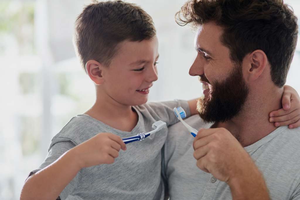 pai com o filho no colo escovando os dentes.