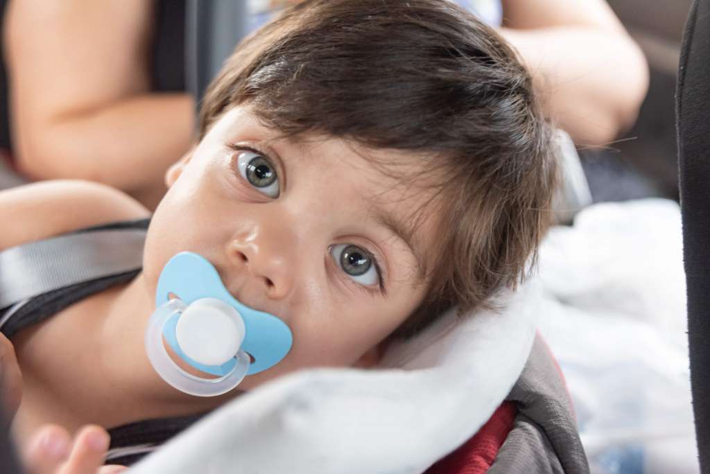 bebê deitado chupando chupeta e olhando para câmera. 