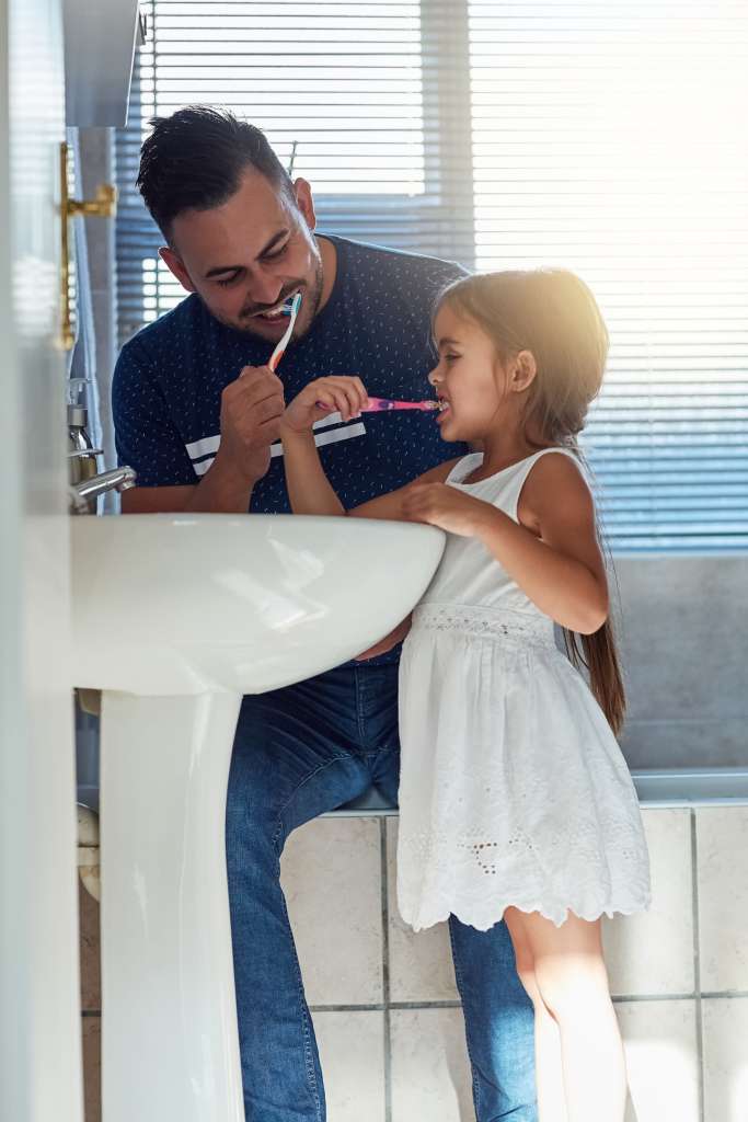 pai e filha escovando os dentes na pia.