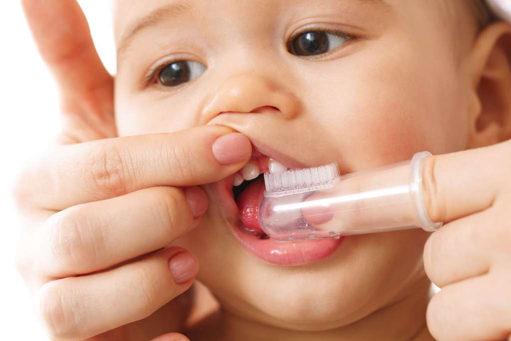 mãe escovando os dentes de leite do bebê com escova de dente especial. Medida preventiva para a cárie na infância.