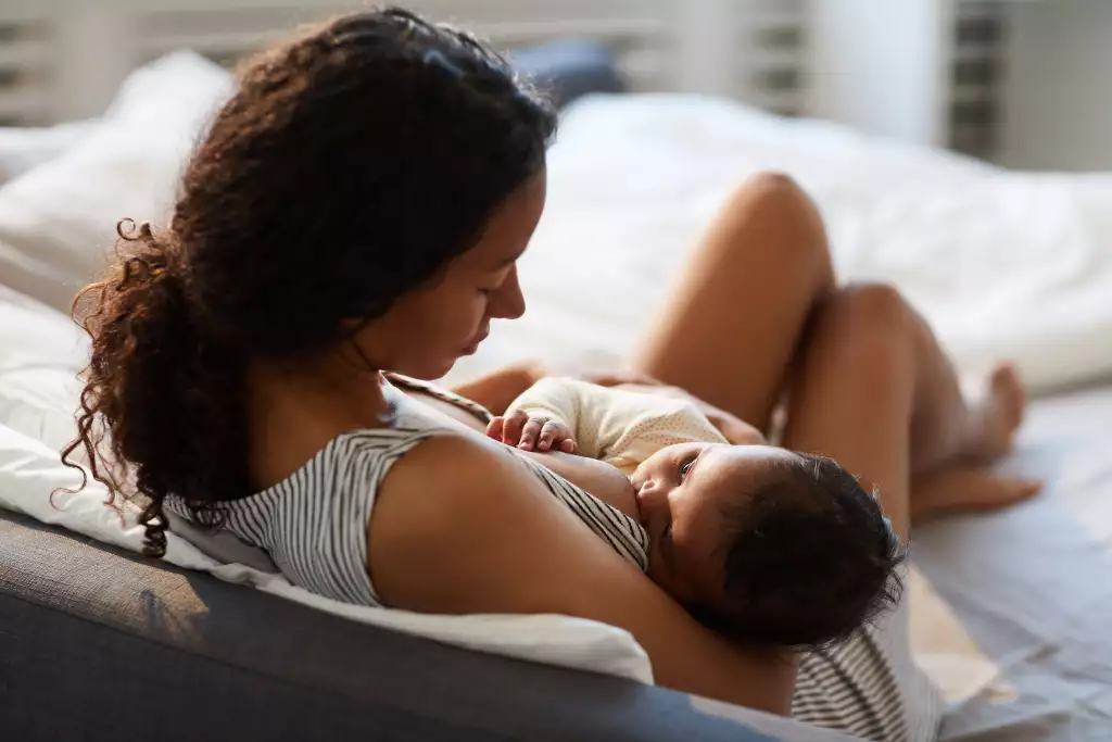 Mãe encostada na cama amamentando seu filho